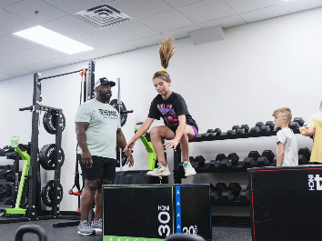Coach cueing a young athlete through a box jump during an Iron Athlete session